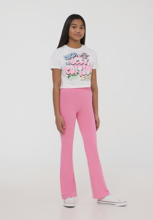 T-shirt bianco corto con grafica testuale colorata, abbinato a leggings rosa a campana. Entrambi i capi sono realizzati in morbido cotone.
