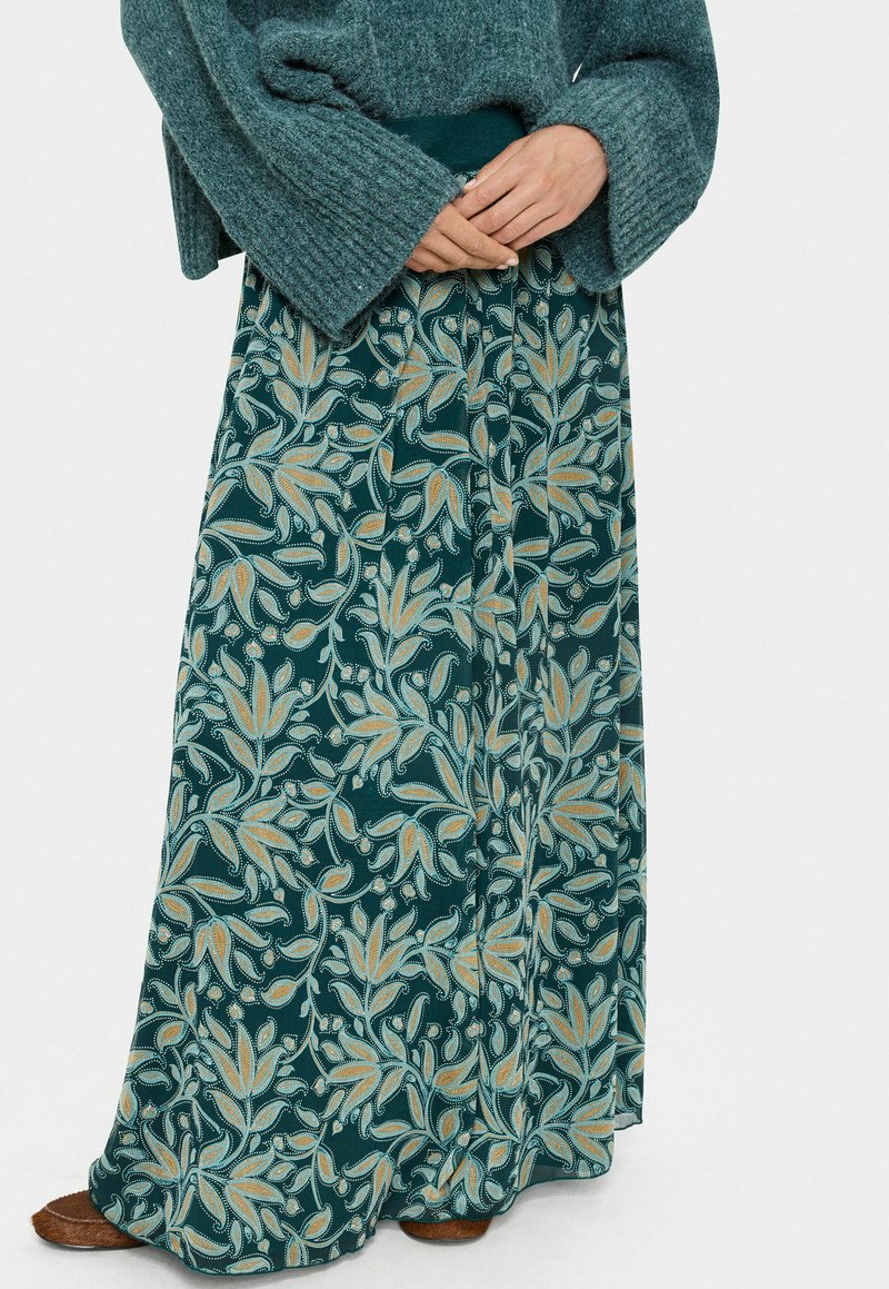 Maxi nederdel med en mørk teal baggrund, der har guld- og lysblå blomster mønstre. Blødt stof med et let design og elastisk talje.