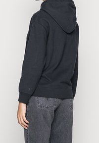 Zwarte hoodie van zacht materiaal, met ribgebreide manchetten en onderrand. Gecombineerd met vervaagde grijze high-waisted spijkerbroek.