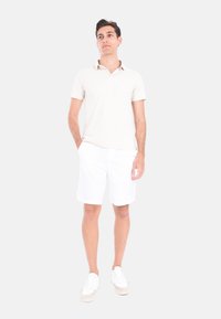 Polo shirt beige chiaro, pantaloni corti bianchi e sneakers bianchi. Vestibilità slim, maniche corte, design casual e texture semplice. Nessun motivo o accento.