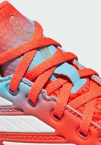 Atletska obuća s teksturiranim, gradijentnim dizajnom u crvenoj i plavoj boji, s istaknutim narančastim vezicama i bijelim akcentima sa strane.