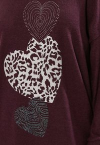 Vinröd sweatshirt med tre hjärtan: övre hjärtat i prickigt silver, mittersta hjärtat i silver leopardmönster, nedersta hjärtat med svarta zebraränder.