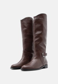Καφέ δερμάτινες μπότες μέχρι το γόνατο με κομψό σχεδιασμό, στρογγυλεμένη μύτη και διακοσμητική αγκράφα στο πλάι. Ομαλή υφή και χαμηλό τακούνι τετράγωνου σχήματος.