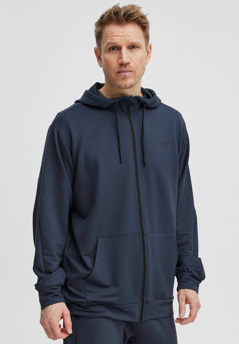 Námořnická mikina na zip vyrobená z hladkého materiálu, s klokaní kapsou, nastavitelnou kapucí se šňůrkou a minimalistickým logem na hrudi.