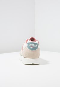 Sneaker Reebok con tomaia in suede di un rosa chiaro e beige, suola bianca e logo teal sul tallone. Forma arrotondata e colletto imbottito.