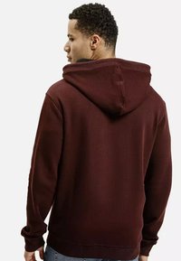 Bordowa bluza z dużym kapturem, ściągaczami przy mankietach i na dolnym wykończeniu. Materiał wydaje się miękki o gładkiej fakturze. Widok z tyłu ujawnia szczegóły szycia.