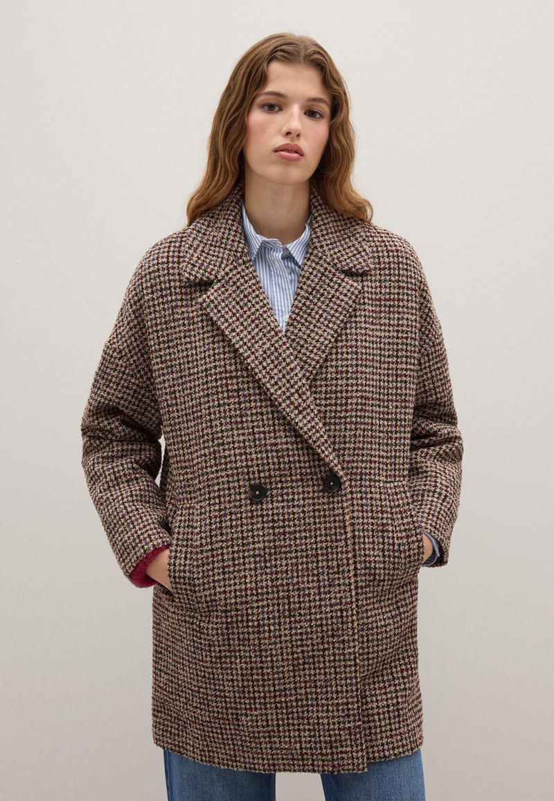 Abrigo de doble botonadura en un estampado de tipo houndstooth en tonos marrón y crema, con grandes solapas muesca y bolsillos laterales, y un interior forrado.