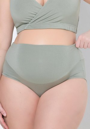 Frau trägt hellgrüne, hoch taillierte Unterwäsche und passendes Wickel-Cropped-Top, hält mit einer Hand den Bund der Unterwäsche.