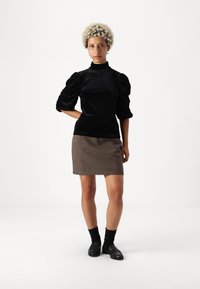 Fekete bársony felső, magas nyakkal és puffos ujjal, kombinálva egy houndstooth mintás szoknyával. A modellen fekete loaferek és zoknik vannak.
