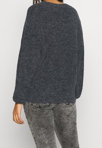 Tmavě šedý pletený svetr s uvolněným střihem, dlouhými rukávy a kulatým výstřihem. Měkká textura s jemným pleteným vzorem.