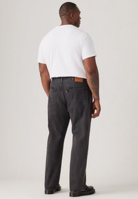 Zwarte denim jeans met een relaxed fit, zichtbare achterzakken en een tan lederen label op de tailleband, gecombineerd met een eenvoudig wit T-shirt.