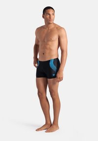 Costume da bagno realizzati in tessuto nero con motivi geometrici blu sui lati; design aderente, lunghezza a metà coscia e texture liscia.