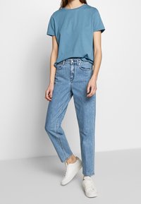 Camiseta de color azul claro con escote redondo, combinada con jeans de mezclilla claros de pierna recta y cintura alta. Zapatillas blancas completan el look.