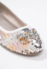 Chaussure plate recouverte de sequins argentés et dorés, avec un groupe de strass clairs sur le bout et une bordure en tissu blanc.