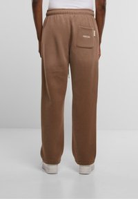 Braune Jogginghose mit lockerer Passform, ausgestattet mit einem elastischen Bund, einer Gesäßtasche und dezentem Branding. Glatte Textur, schlichtes Design.