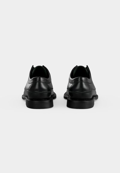 Paire de chaussures habillées en cuir noir vues de dos sur un fond blanc uni.