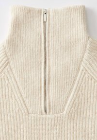 Pullover a coste beige con colletto alto e una cerniera argentata che scende lungo la schiena, caratterizzato da un design testurizzato sul tessuto.