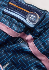 Bouton en plastique transparent fixé sur un tissu bleu à motifs avec des rayures cousues bleu clair et orange et une bordure en ruban rose.