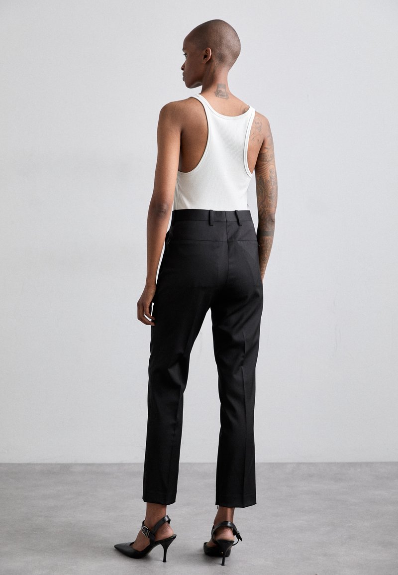 Black tailored trousers with a slim fit, paired with a white ribbed tank top; features a high waist and ankle-length cut.