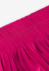 Fuchsia plisserad kjol med samlad elastisk midja, mjuk textur och flytande design som visar framträdande vertikala veck.