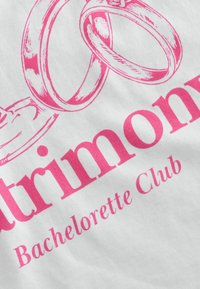 Vitt tyg med rosa tryckt text som säger "Matrimony Bachelorette Club," åtföljt av illustrerade ringar ovanför texten.