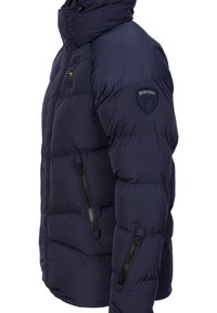 Granatowa kurtka puchowa z wysokim kołnierzem, pikowaniem izolującym, kieszeniami na zamek i naszywką z logo na lewym ramieniu.