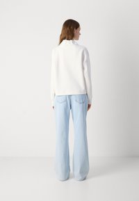 Felpa bianca con colletto alto, caratterizzata da una vestibilità comoda. Abbinata a jeans a gamba ampia di colore azzurro chiaro, che presentano una texture morbida e dettagli minimi.