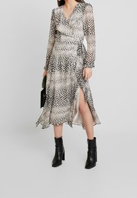 Wickelkleid aus transparenter, tierischer Druckstoff mit langen Ärmeln, einem tiefen V-Ausschnitt und einem Oberschenkel-spalt, kombiniert mit schwarzen Stiefeletten.
