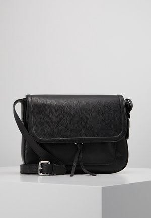 Sac bandoulière en cuir noir avec sangle réglable, rabat avant et finition texturée subtile sur surface d'exposition blanche.