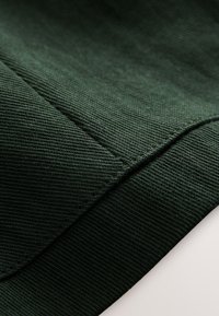 Tissu côtelé vert foncé en gros plan montrant une couture détaillée le long d'une couture avec un bord plié sur fond blanc.