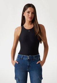 Bodysuit negro sin mangas con escote redondo, que presenta un pequeño logotipo triangular en el centro y se combina con unos vaqueros de cintura alta azules.