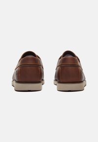 Braune Lederschuhe mit flachem Profil, beiger Gummisohle, kontrastierenden Nähten und runder Zehenpartie. Die Rückansicht zeigt eine glatte, polierte Oberfläche.