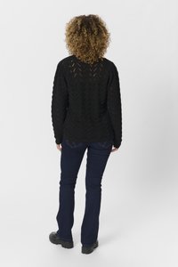 Maglione nero a maglia con motivo testurizzato e maniche lunghe, abbinato a pantaloni flare in denim scuro e stivali neri chunky.