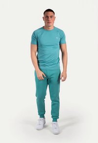 Turkusowy zestaw sportowy z dopasowaną koszulką z krótkim rękawem i spodniami dresowymi. Gładka faktura, elastyczna talia i białe trampki.