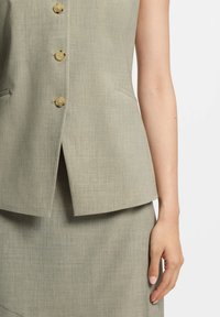 Jasnoszara, teksturowana kamizelka z dekoltem w serek, sześć kremowych guzików i kieszenie boczne, noszona na pasującej spódnicy.