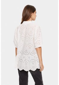 Weiße Baumwollbluse mit Broderie Anglaise Details, kurzen Puffärmel und einem gerafften Ausschnitt. Verfügt über einen gewellten Saum und ein Peplum-Design.