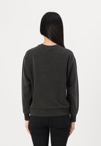 Sweatshirt grigio scuro con collo rotondo, maniche lunghe e polsini e orlo a coste. Il tessuto sembra morbido con una finitura testurizzata.