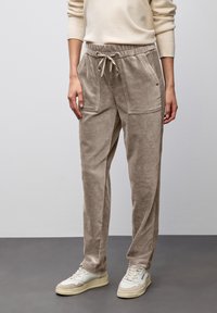 Kvinna i beiga kordflodpants med framfickor och mudd i midjan, kombinerat med en krämfärgad tröja och vita sneakers.