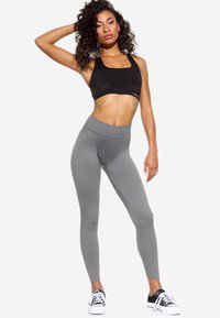 Reggiseno sportivo nero a coste con scollatura quadrata, abbinato a leggins grigi a vita alta. Il modello indossa scarpe da ginnastica nere e bianche.