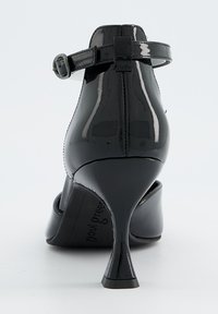 Chaussure noire à talons hauts avec une finition brillante, dotée d'une bride à la cheville et d'un talon fin, sur fond uni.