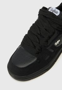 Melni sporta apavi, kuri izgatavoti no gludas ādas un teksturēta auduma. Iezīmējas ar bieziem, pinumiem līdzīgiem šņorēm un zīmola akcentu sānos.