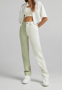 Pantalones bicolores en verde claro y blanco con un diseño de pierna recta, hechos de algodón. Combinados con una camisa blanca de botón recortada y zapatillas blancas.