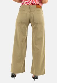 Pantalones de pierna ancha en khaki con una textura suave, que cuentan con dos bolsillos traseros, un parche de cuero con la palabra "PLEASE" y un pequeño detalle en forma de corazón.
