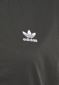 Svart tyg med en fin ribbad textur som har en vit broderad Adidas-logotyp och tre-stripes accent under logotypen.