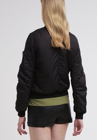 Svart bomberjacka med en mjuk textur, ribbade muddar och nederkant, samt en blixtlåsficka på ärmen. Matchad med olivgröna shorts med midjeband.