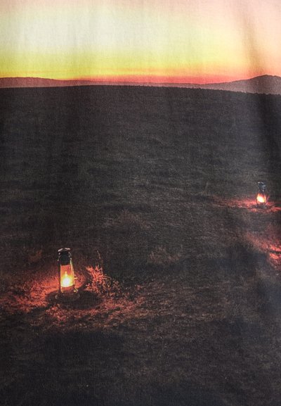 Un tissu sombre avec un paysage imprimé, présentant un dégradé de coucher de soleil allant du jaune à l'orange, et deux lanternes lumineuses au premier plan.