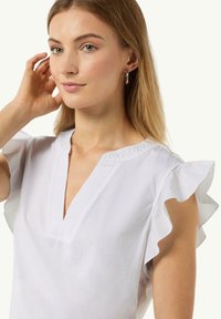 White blouse with ruffled sleeves, V-neckline, and textured trim. Made from soft fabric, it features a lightweight and breathable design.