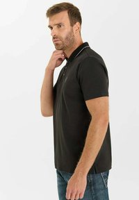 Zwarte polo met een kraag, korte mouwen en witte accentstiksels. De stof lijkt glad, aansluitend en lichtgewicht.