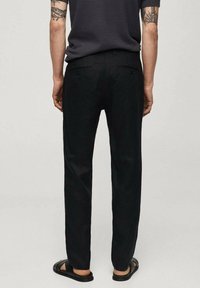 Pantaloni neri a taglio dritto con una texture liscia, due tasche posteriori e una cintura. Indossati con sandali neri.