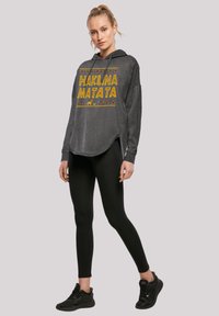 Grå langermet hettegenser har teksten "HAKLINA MATATA" i gult med trekantakenter. Kombinert med svarte tights og sneakers.
